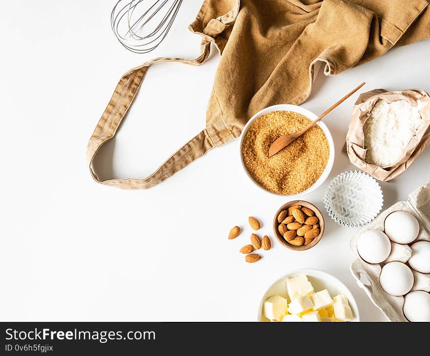 Ocher apron and various baking ingredients - flour, eggs, sugar, butter, nuts on white background. Top view