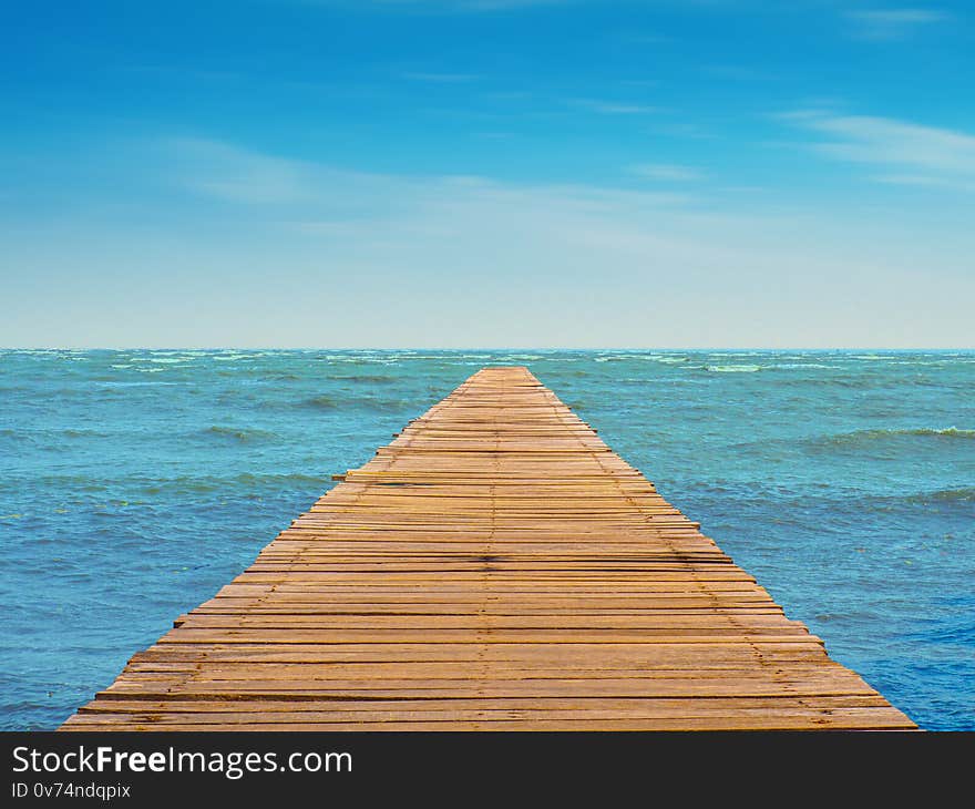 View of seascape with wooden walkway leading to the blue sea and beautiful cloudy skies. View of seascape with wooden walkway leading to the blue sea and beautiful cloudy skies