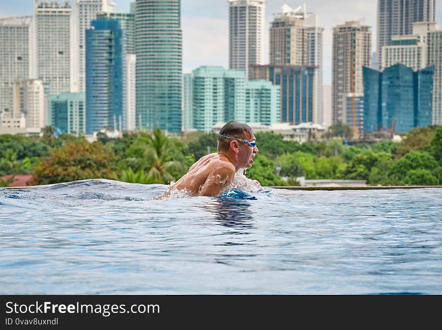 A man swims a butterfly in a pool on the roof of a luxury hotel. View of the city of Manila from the pool of the luxury five-star Discovery Primea hotel. Sunny weather. Skyscrapers on the background. A man swims a butterfly in a pool on the roof of a luxury hotel. View of the city of Manila from the pool of the luxury five-star Discovery Primea hotel. Sunny weather. Skyscrapers on the background