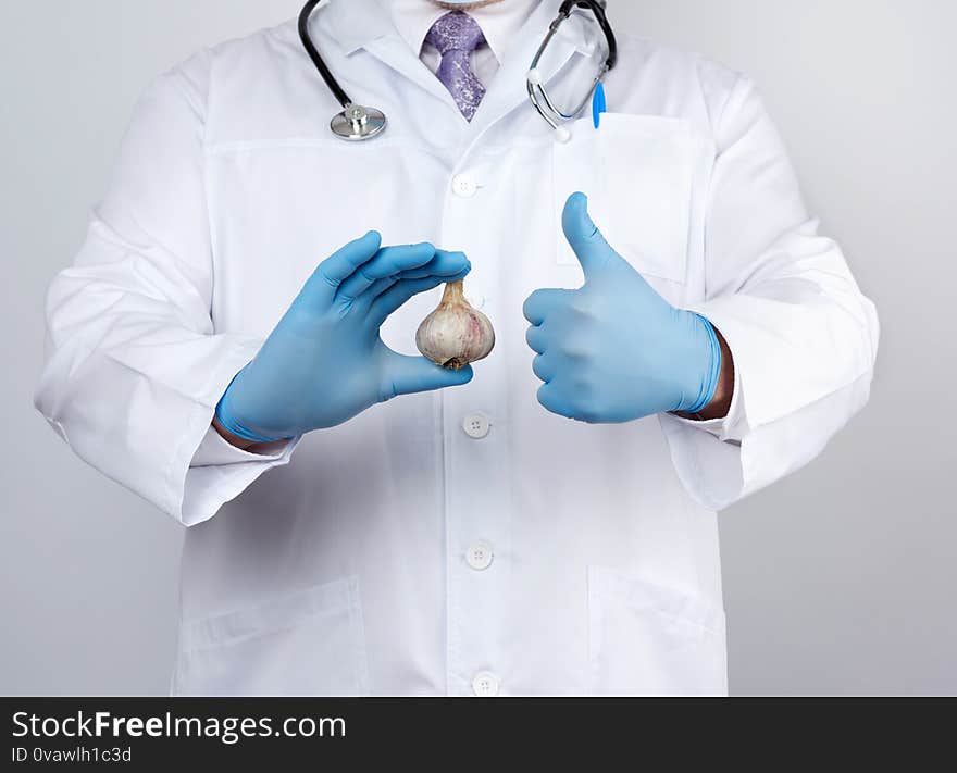 Doctor in a white medical coat and blue rubber gloves holds a fresh head of garlic, prevention against viral diseases