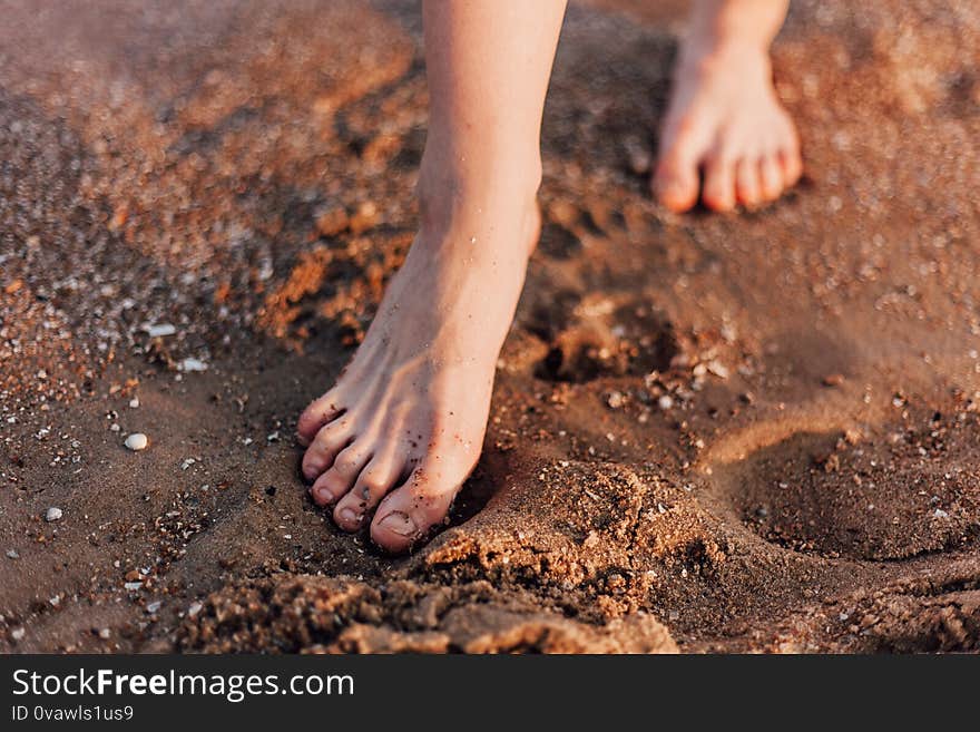 Women`s feet walk on the sand on the beach