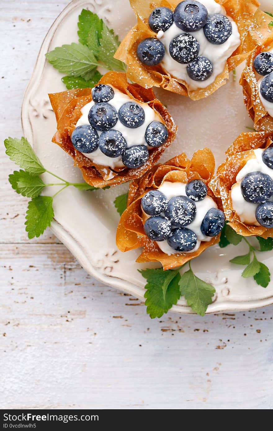 Phyllo cups with Mascarpone cheese filling topped with fresh blueberries sprinkled with powder sugar on a white plate top view, close up view. Delicious filo pastry dessert. Phyllo cups with Mascarpone cheese filling topped with fresh blueberries sprinkled with powder sugar on a white plate top view, close up view. Delicious filo pastry dessert