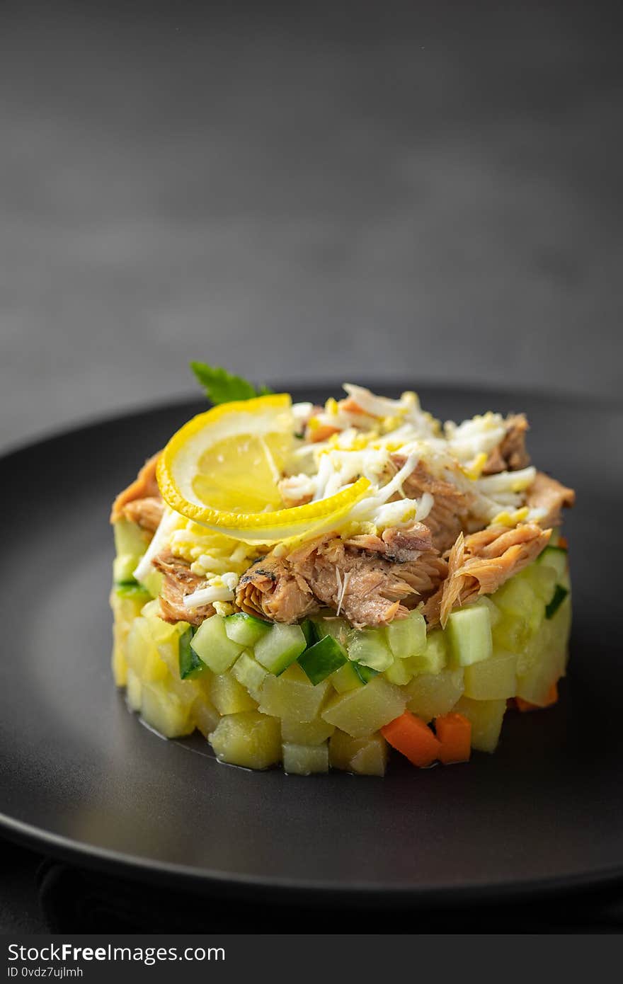 Salad with canned tuna and vegetables in culinary ring on black plate. Dark background. Beautiful serving in the restaurant