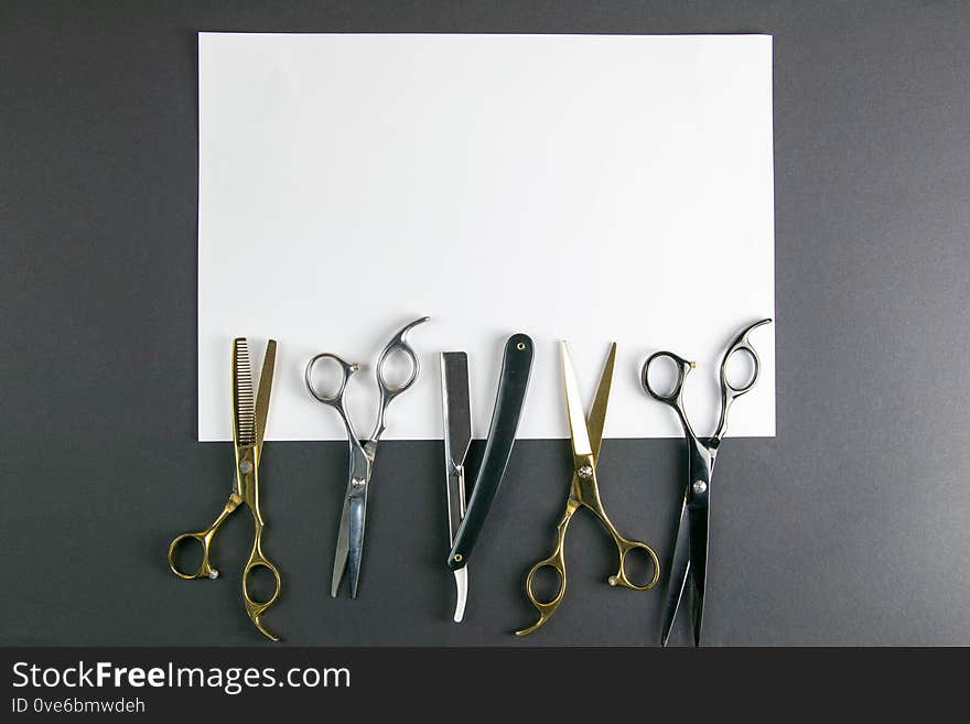 Scissors, hair clipper, combs, dangerous razor on a white sheet on black background. Hairdressing concept