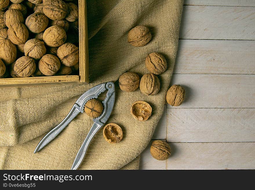 Walnuts In A Wooden Box, Which Stands On An Old Rustic Sack, Also Scattered On A White Table Nearby Is A Cracker Of Walnut