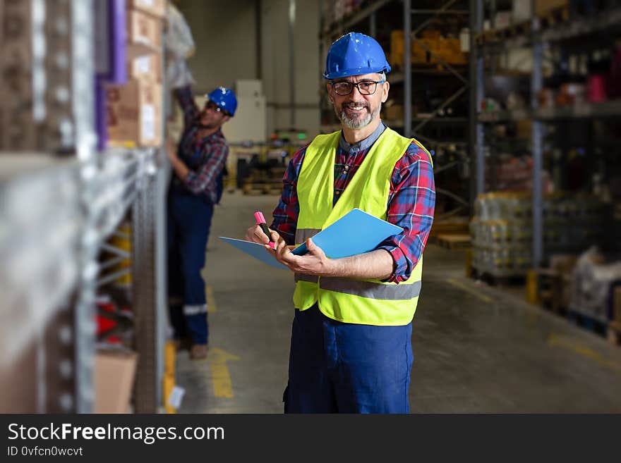 Old Warehouse manager writing on clipboard in a large warehouse