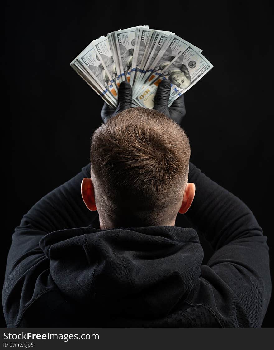 Business and finances concept. Man in black hoody holding pack of american dollars over black background