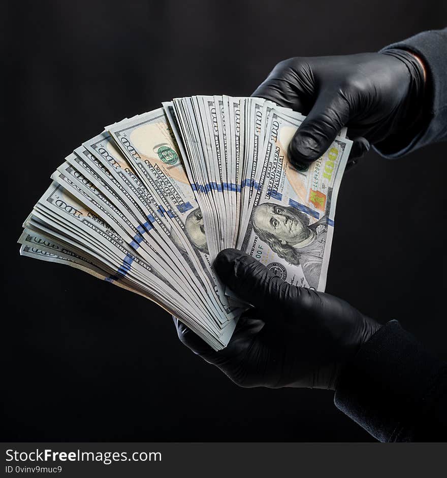 Finances concept. Man in black gloves holding pack of dollars over black background