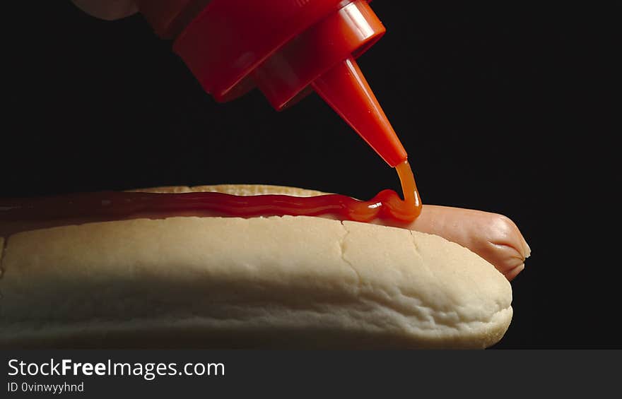 CLOSE UP: Ketchup bottle pouring tomato sause on a hot dog with sausage. Side view