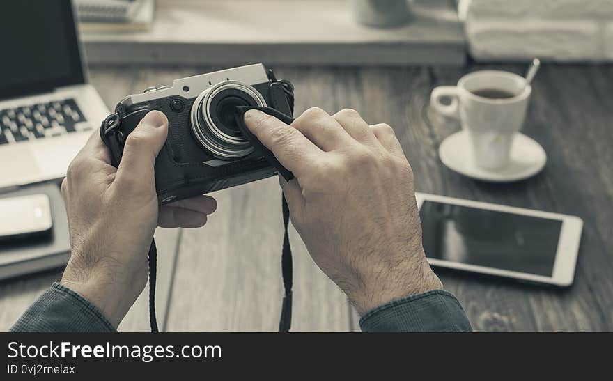 Hipster photographer at home sitting at desk and cleaning his camera lens with a cloth, point of view shot