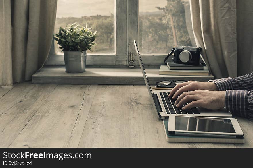 Hipster man working with a laptop and a tablet in front of a window in a rustic vintage house. Hipster man working with a laptop and a tablet in front of a window in a rustic vintage house