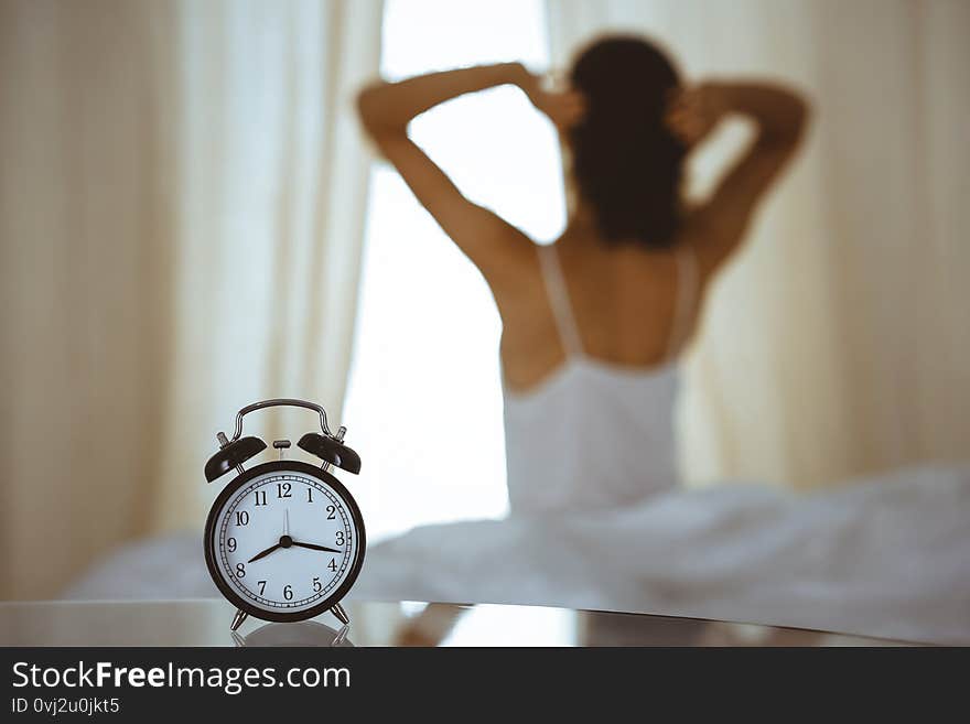 Woman stretching hands in bed after wake up, sun flare . Brunette entering a day happy and relaxed after good night sleep and back view. Concept of a new day and joyful weekend.