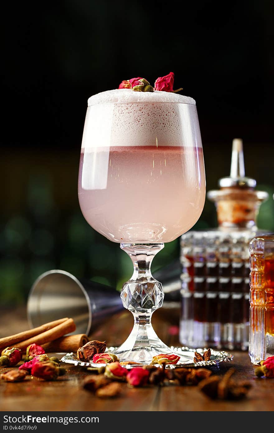 Female pink cocktail with foam in a glass. decorated with dried rose. in the background is visible barman inventory. Female pink cocktail with foam in a glass. decorated with dried rose. in the background is visible barman inventory