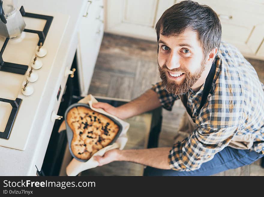 Bearded young man taking heart shaped cake out of the oven