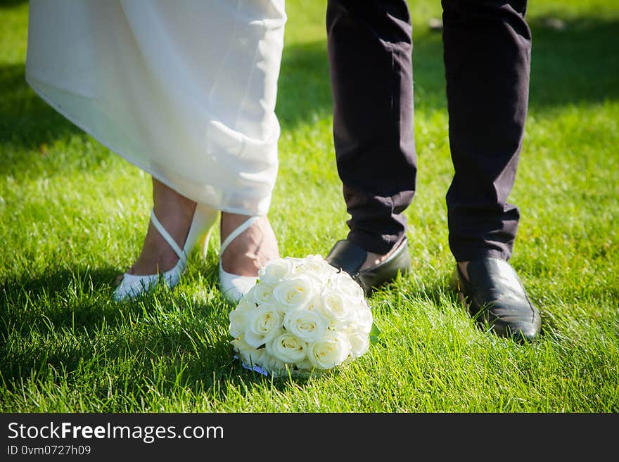 Wedding bouquet of the bride and feet newlyweds