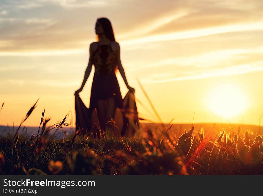 Young beautiful girl in a light summer dress with a husky dog posing in backlit sunset standing barefoot