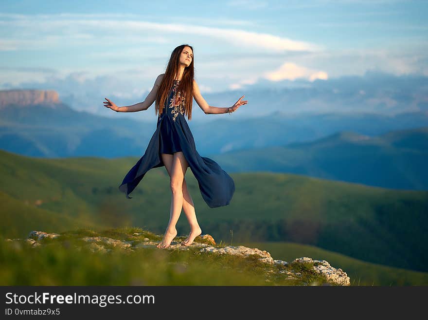 A young girl dancing on top of a mountain, against the backdrop of Caucasian ridge during sunset