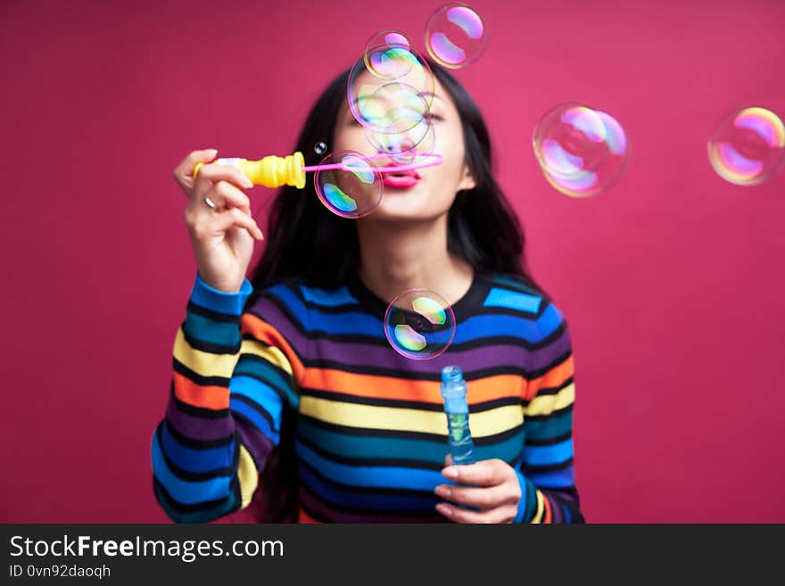 Happy beautiful woman blowing soap bubbles isolated over pink background