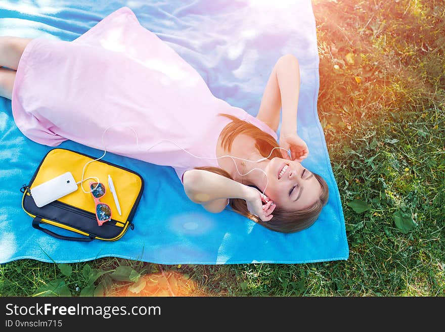 Online media entertainment. Music streaming. Top view of pretty woman relaxing on grass in park listening to music.
