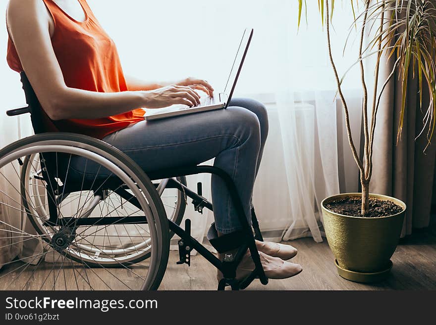 Woman in a wheelchair at home with a laptop on her lap, hand close up, unrecognizable man