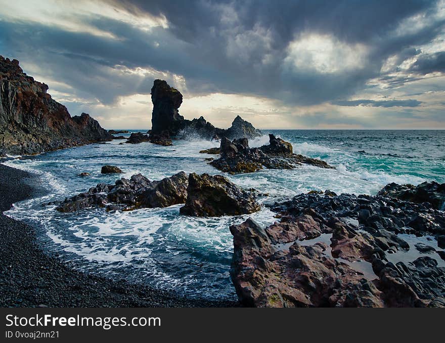 Dramatic shot of stormy coastline with black rocks and high waves on Snaefellsnes peninsula Iceland. Black clouds on sky, turquoise water. No people visible