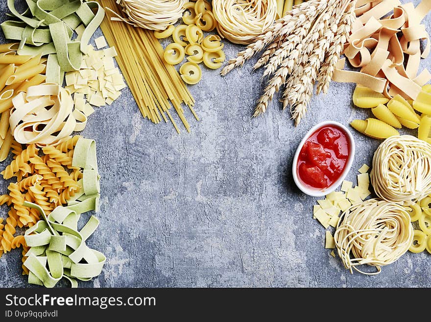 Mixed types and shapes of italian pasta on grey stone, background