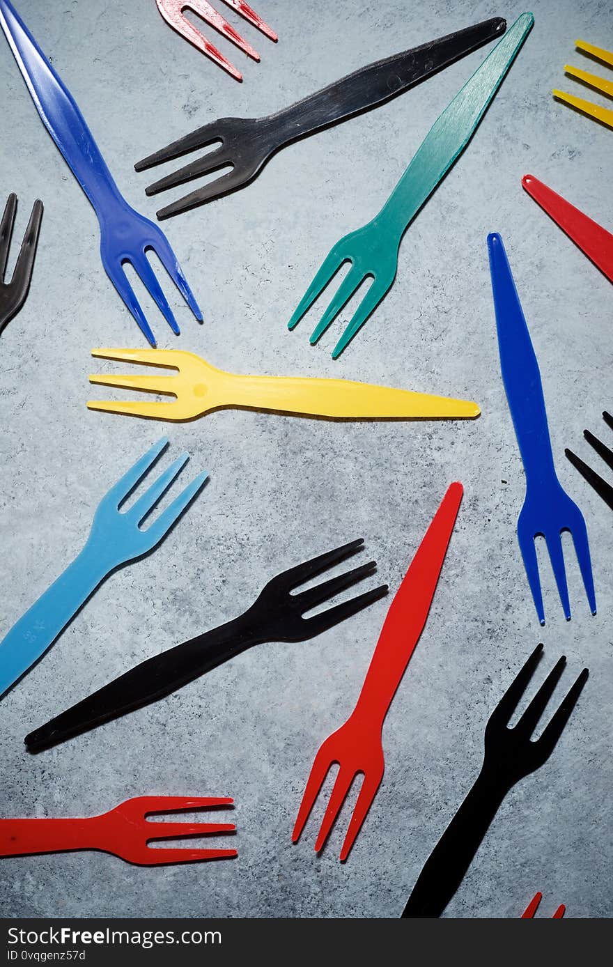 Multicolored plastic cutlery on a stone table. Multicolored plastic cutlery on a stone table