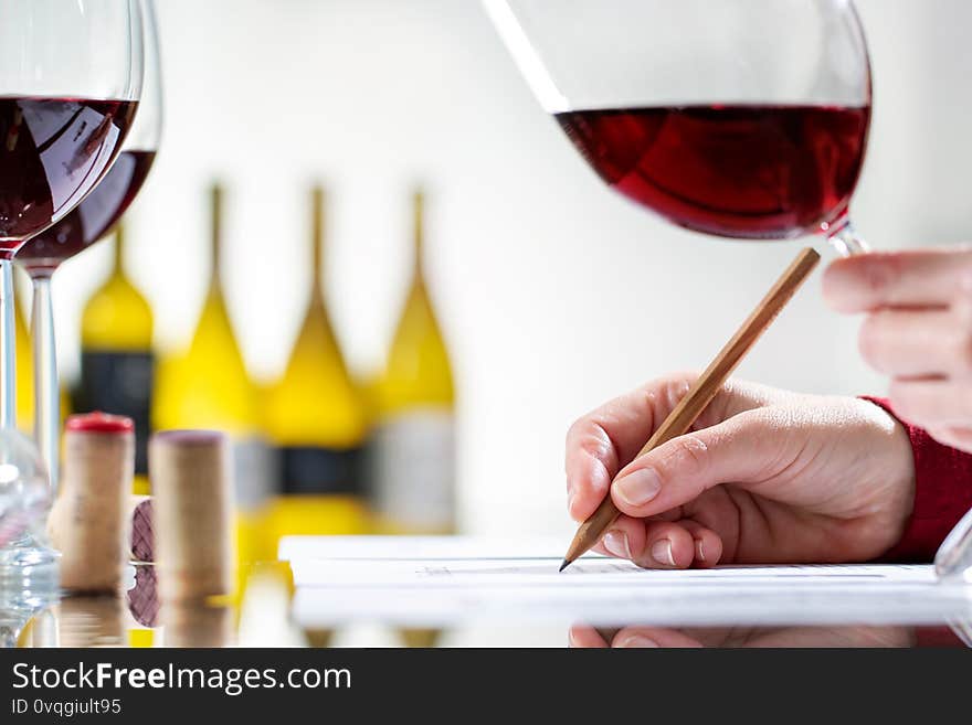 Close up detail of enologist writing notes on wine evaluation at table. Out of focus bottles in background. Close up detail of enologist writing notes on wine evaluation at table. Out of focus bottles in background