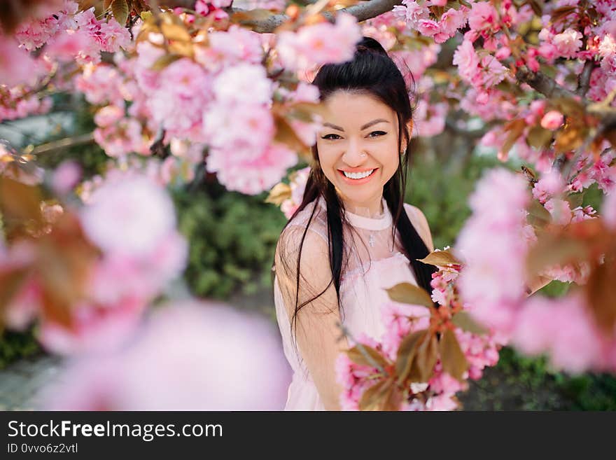 Portrait of young woman in park with blooming sakura trees