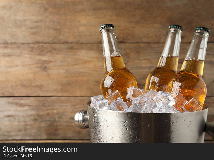 Metal bucket with beer and ice cubes on wooden background. Space for text