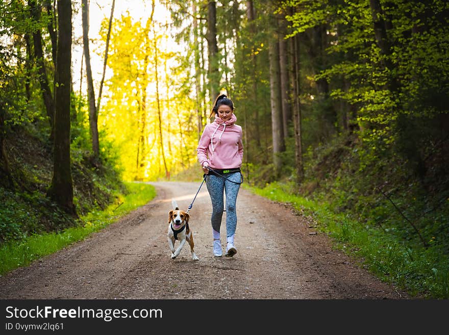 Young woman and dog running together on country in forest. Cheerful female exercising outdoor with her pet. Active people concept