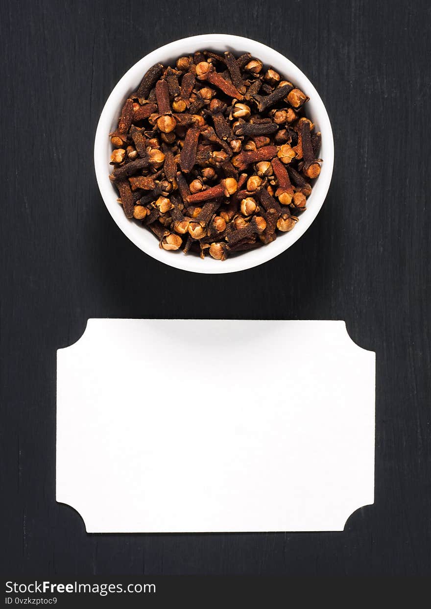 Spice cloves powder in white ceramic bowl and inscription plate on black wooden background, copy space