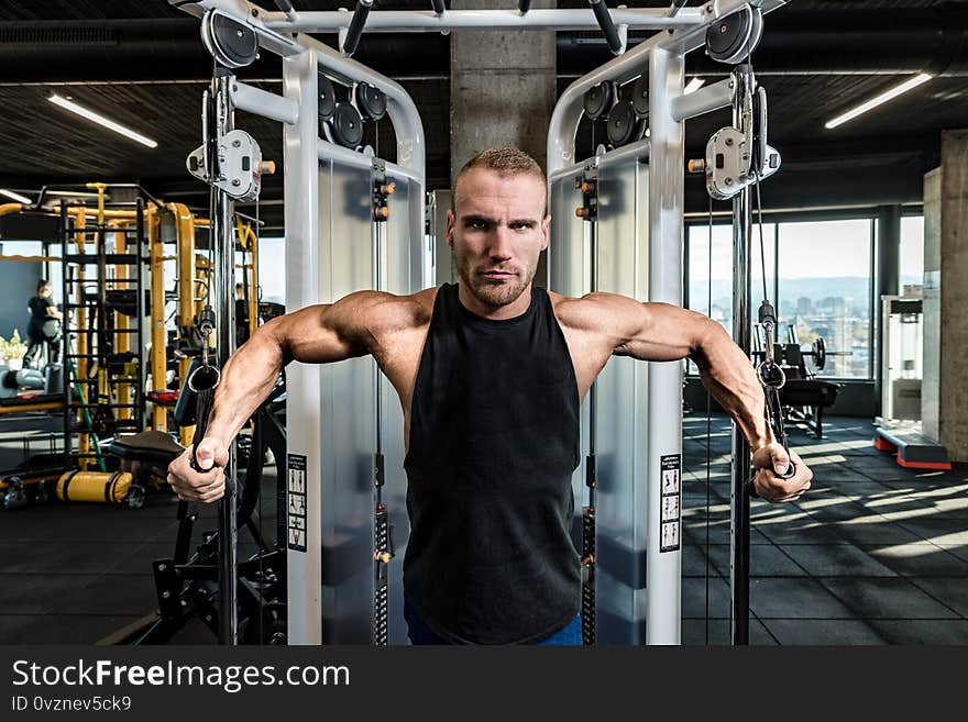 Young active strong sweaty focused fit muscular bodybuilder man chest muscles stretching workout on cable machine in the gym