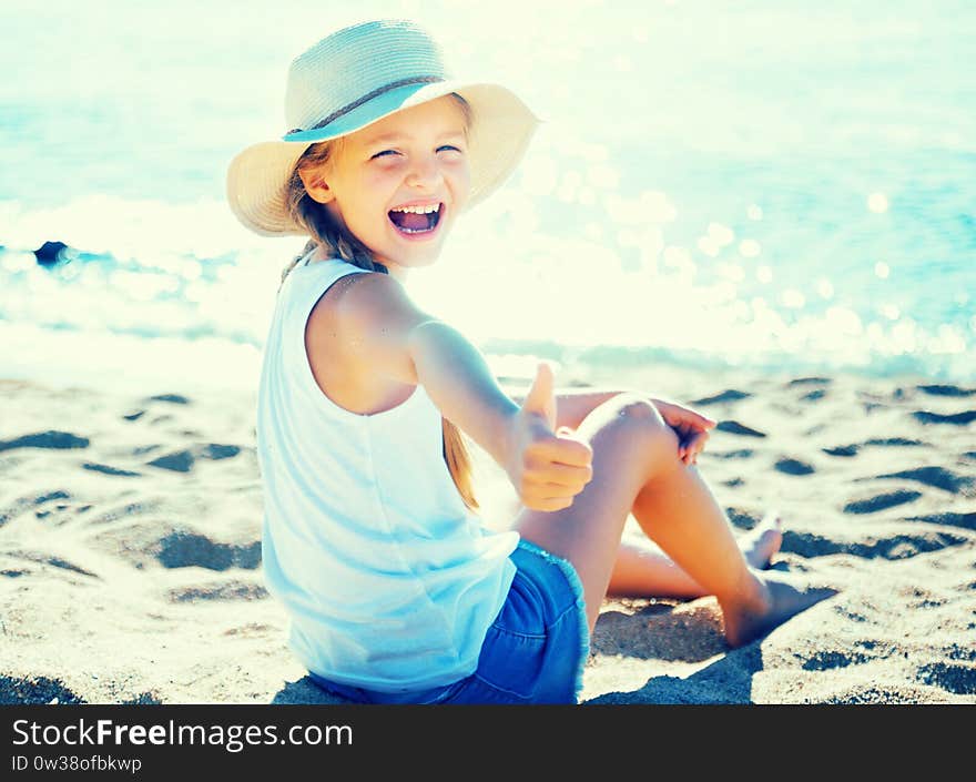 Child in hat on beach shows thumb up