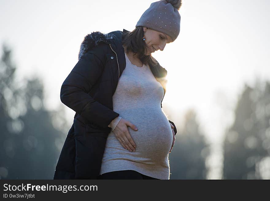 View from below of a pregnant young woman standing outside in nature, lovingly looking down at her swollen belly touching it gently. View from below of a pregnant young woman standing outside in nature, lovingly looking down at her swollen belly touching it gently