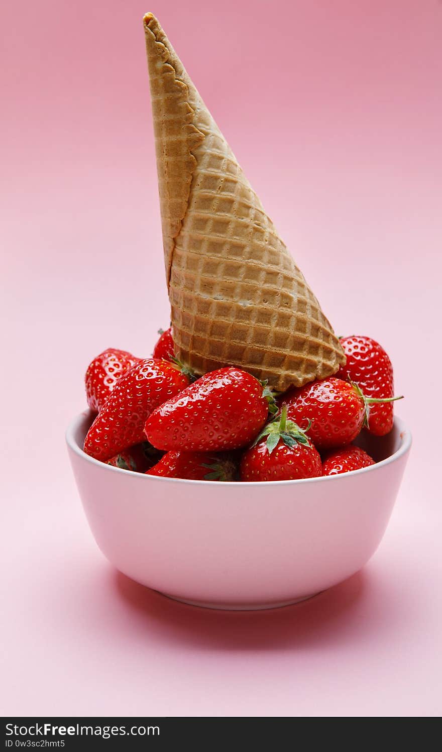 Ice cream cone on fresh strawberries in a bowl on pink background.