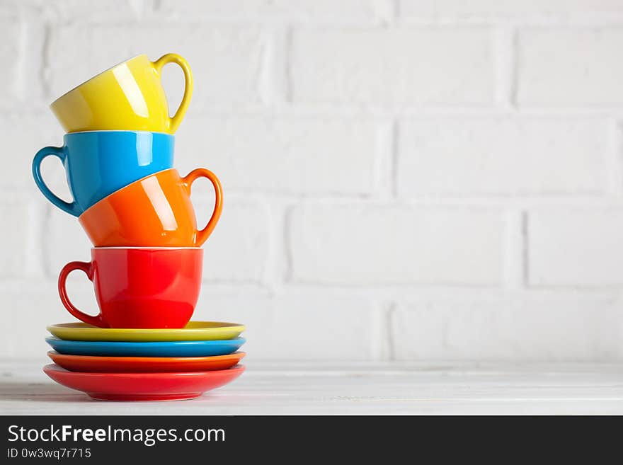 Colorful cups on the white background of a brick wall. Background with copy space. Horizontal. Selective focus.