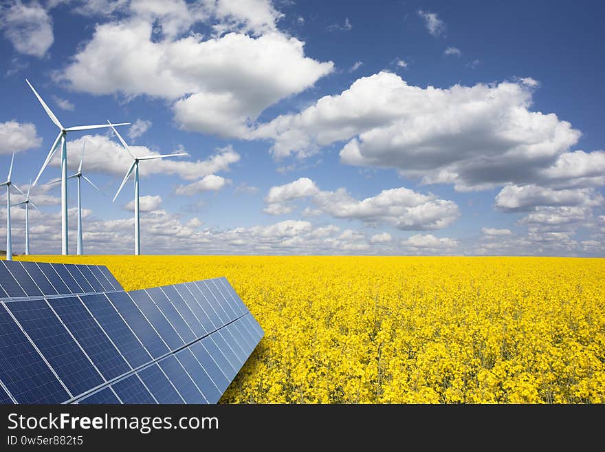 Renewable or green energy concept with wind turbines solar panels and yellow raps field on blue sky with white clouds