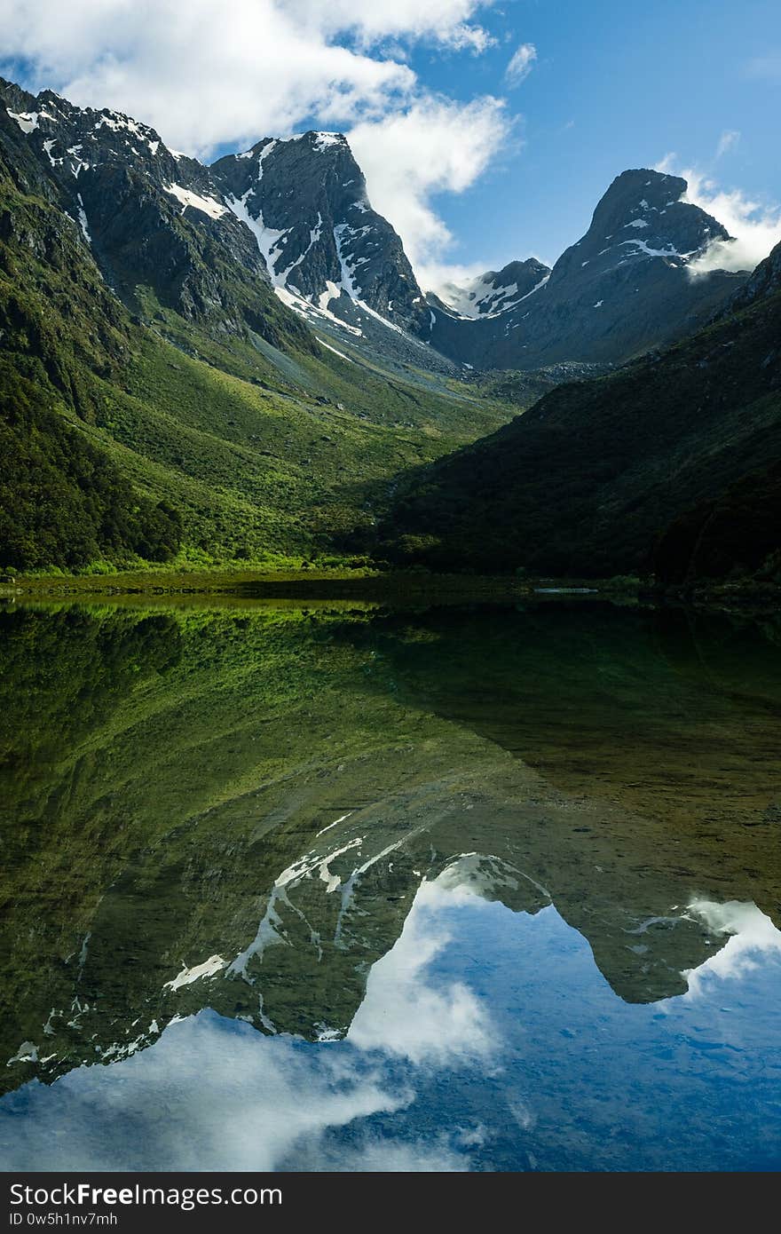 Vertical Shot Of The Water Reflecting The Mountains Under The Blue Sky