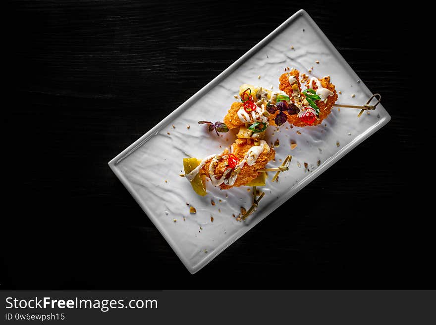 Spicy fried shrimp skewers served on plate on black wooden table background