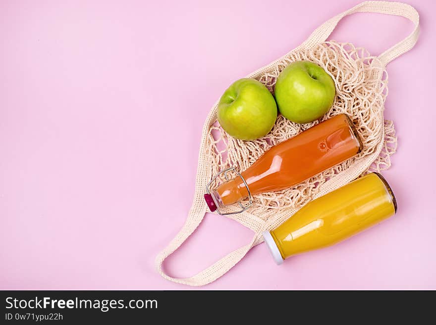 Bag with Two Bottles of Citrus Juice Green Apples Diet Food Top View Horizontal Pink Background.