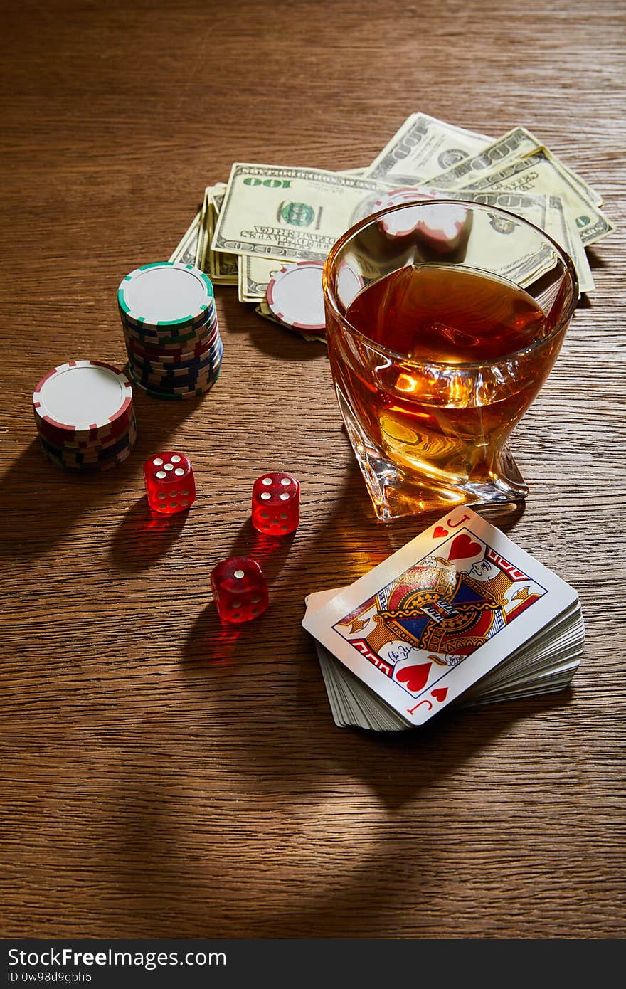 Angle view of glass of cognac near dollar banknotes, playing cards, casino chips and dice on wooden background