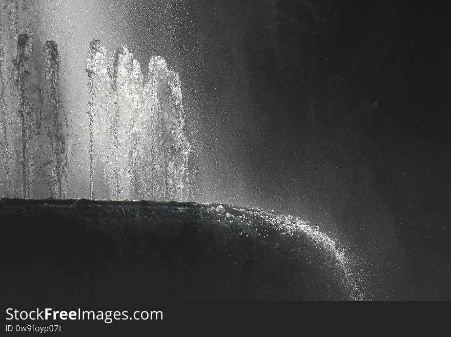 Detail of backlit refreshing water flowing in a fountain in spring against sunlight creating beautiful reflections and splashes. Fountain at Cairoli square at the Castello Sforzesco in Milan, Italy. Detail of backlit refreshing water flowing in a fountain in spring against sunlight creating beautiful reflections and splashes. Fountain at Cairoli square at the Castello Sforzesco in Milan, Italy