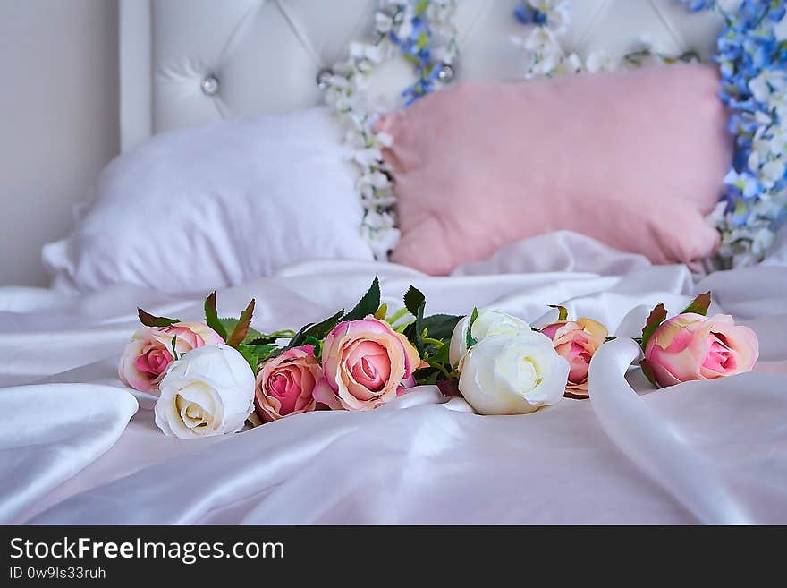 A bouquet of artificial flowers lies on a white silk blanket on a large bed.