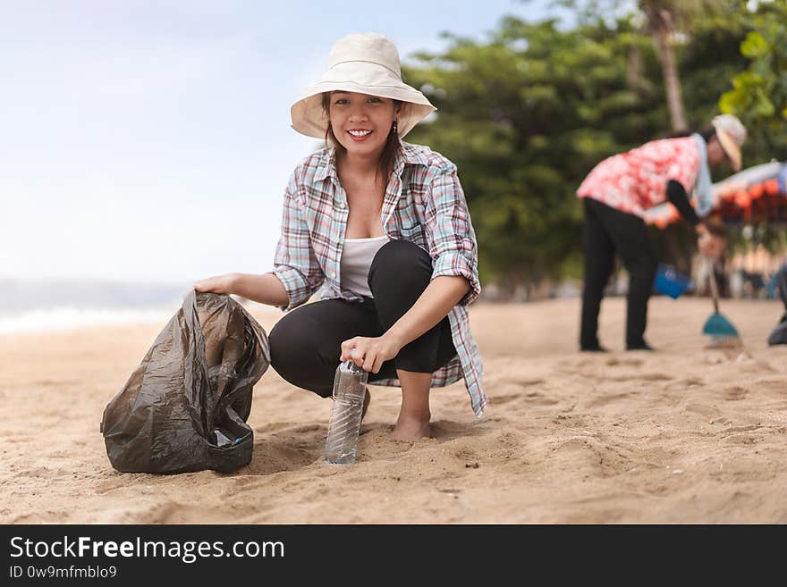 Asian woman picking  bottle into plastic bag black for cleaning the beach in morning time, Volunteer concept.