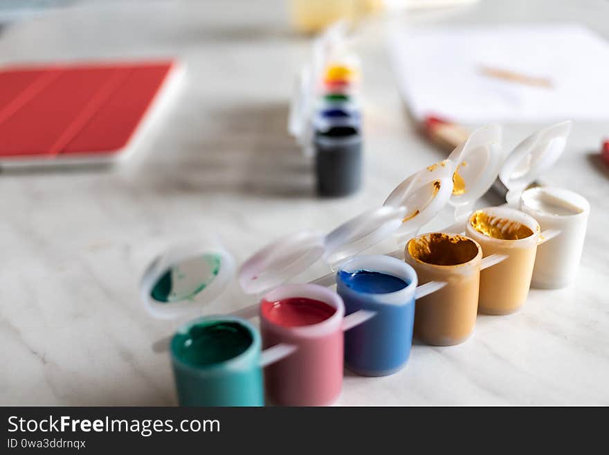 Different colors of paint on a light table. on the table is a tablet with a red cover. there is a drawing sheet in the distance. natural light and shadows. Different colors of paint on a light table. on the table is a tablet with a red cover. there is a drawing sheet in the distance. natural light and shadows