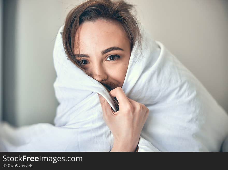 Close up of smiling attractive young lady having rest in bed and looking for camera at her home. Close up of smiling attractive young lady having rest in bed and looking for camera at her home