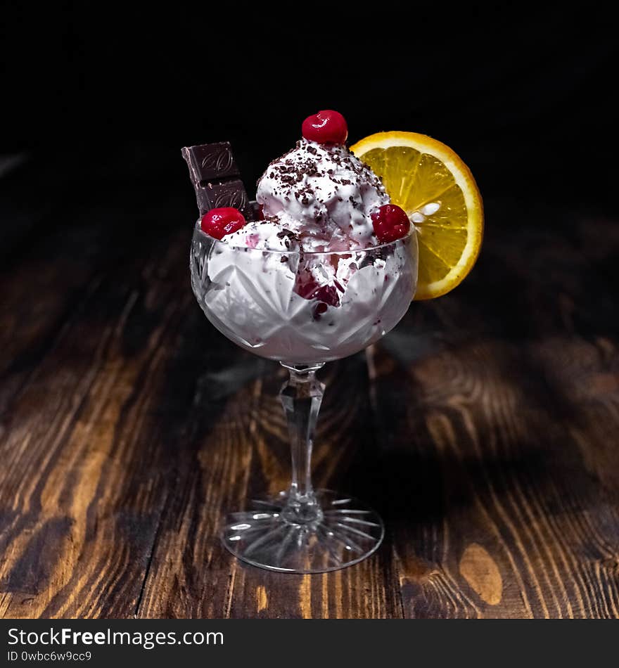 Ice cream with chocolate, cherry and orange in a crystal glass. Closeup of colorful ice cream on dark background. Summer concept. Red berry closeup. Concept of product design