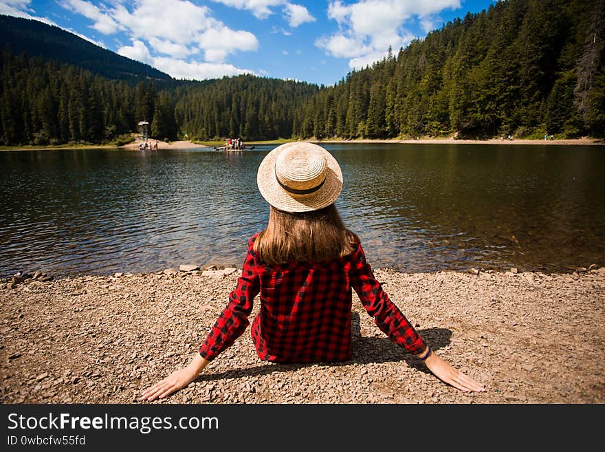 Tourist woman in hat sitting backwards and watching magic lake in mountainous country landscape