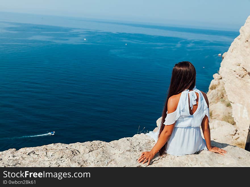 Beautiful tanned woman in blue dress on top of a cliff by the sea